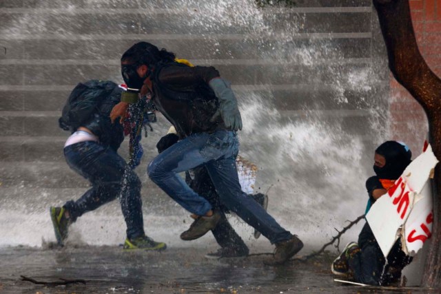 Anti-government protesters run from police water cannon in Caracas