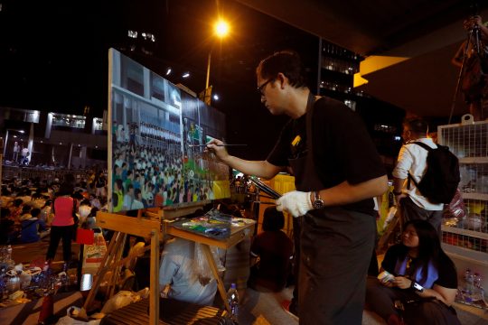A man paints the scene of protesters and riot police during a rally attended by thousands in front of the government headquarters in Hong Kong