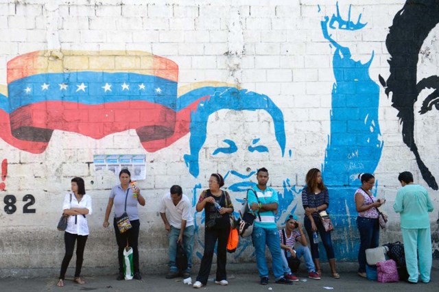 People line up in front of a propaganda graffiti depicting late Venezuelan President (1999-2013) Hugo Chavez (L),  on a wall of the Petare shantytown in Caracas on December 1 , 2015. Sixteen years into late president Hugo Chavez's leftist "revolution," opinion polls indicate the opposition is poised to win legislative elections Sunday for the first time since the firebrand leader came to power.  AFP PHOTO/FEDERICO PARRA / AFP / FEDERICO PARRA