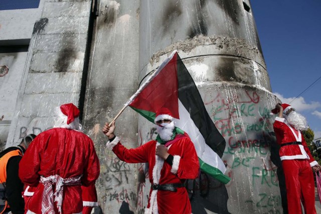 Palestinians dressed up as Santa Claus demonstrate in front of the Israeli controversial separation wall in the West Bank city of Bethlehem, on December 18, 2015.  AFP PHOTO / THOMAS COEX / AFP / THOMAS COEX