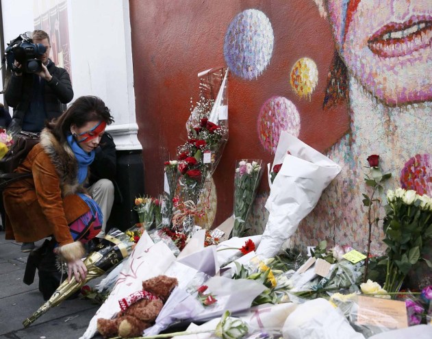 A woman wearing Ziggy Stardust style make-up reacts leaves a bouqet as she visits a mural of David Bowie in Brixton, south London, January 11, 2016. David Bowie, a music legend who used daringly androgynous displays of sexuality and glittering costumes to frame legendary rock hits "Ziggy Stardust" and "Space Oddity", has died of cancer.  REUTERS/Stefan Wermuth