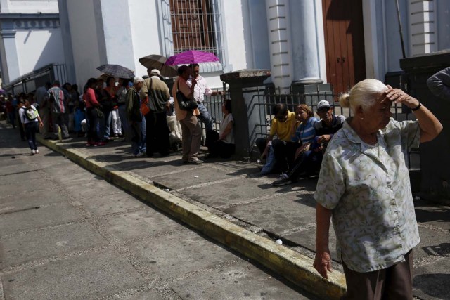 A woman shields herself from the sun, while people wait in a line for the elderly outside a PDVAL, a state-run supermarket, to buy chicken in Caracas January 22, 2016.  Venezuela's opposition refused on Friday to approve President Nicolas Maduro's "economic emergency" decree in Congress, saying it offered no solutions for the OPEC nation's increasingly disastrous recession. Underlining the grave situation in Venezuela, where a plunge in oil prices has compounded dysfunctional policies, the International Monetary Fund on Friday forecast an 8 percent drop in gross domestic product and 720 percent inflation this year. REUTERS/Carlos Garcia Rawlins