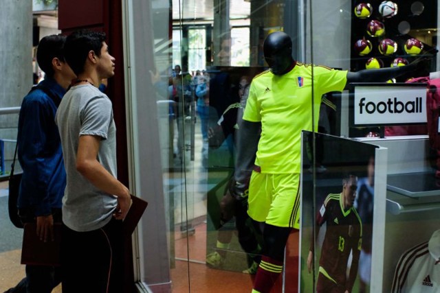 People look at a mannequin dressed in the Venezuelan national football team alternative uniform at a mall in Caracas, on June 16, 2016. Supporting the national football team has become expensive for Venezuelans. / AFP PHOTO / FEDERICO PARRA / TO GO WITH AFP STORY BY ESTEBAN ROJAS