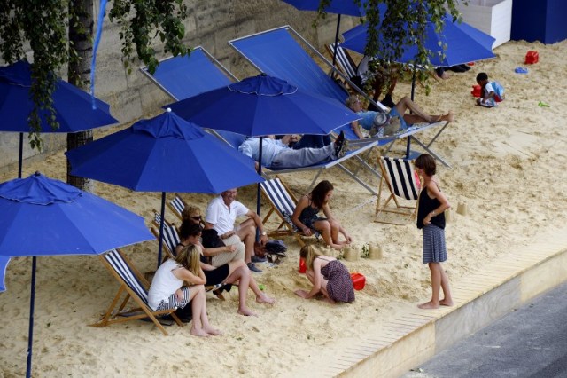 People relax under parasols in "Paris Plage" (Paris Beach) during the opening day of the event on the bank of the Seine river, in central Paris, on July 20, 2016. The 15th edition of Paris Plage will run until September 4, 2016. / AFP PHOTO / BERTRAND GUAY