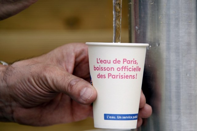 A picture taken in central Paris, on July 20, 2016 in Paris Plage (Paris Beach) shows a man taking water in a cup reading "Paris water, the Parisians official drink". The 15th edition of Paris Plage will run until September 4, 2016. / AFP PHOTO / BERTRAND GUAY