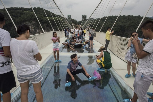 A tourist poses for a photograph on the world's highest and longest glass-bottomed bridge above a valley in Zhangjiajie in China's Hunan Province on August 20, 2016. / AFP PHOTO / FRED DUFOUR