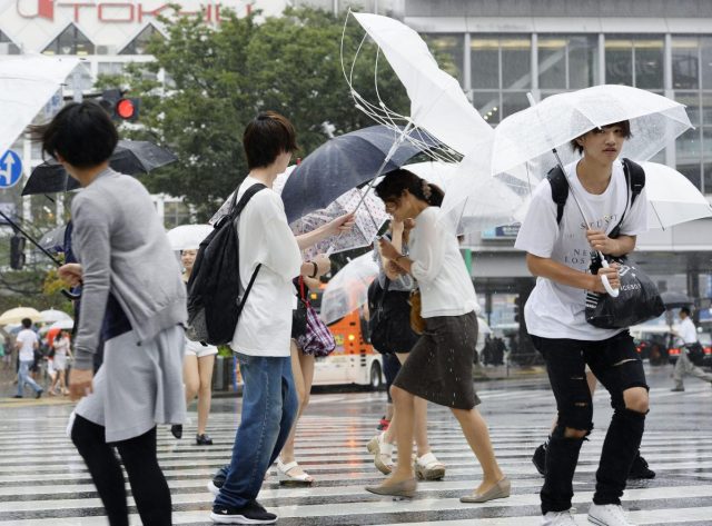 Un grupo de personas camina por una intersección protegidos de los fuertes vientos provocados por el tifón Mindulle, en Tokio, el 22 de agosto de 2016. (Akiko Matsushita/Kyodo News via AP)