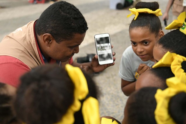 Blind Brazilian photographer Joao Maia explains to some children how he takesc pictures with his smartphone using the sound as a reference during the Rio 2016 Paralympic Games in Rio de Janeiro, Brazil on September 9, 2016. 41-year-old Maia lost his sight at age 28 due to an affection of the uvea. This is the first sportive event y covers as a photographer. / AFP PHOTO / CHRISTOPHE SIMON