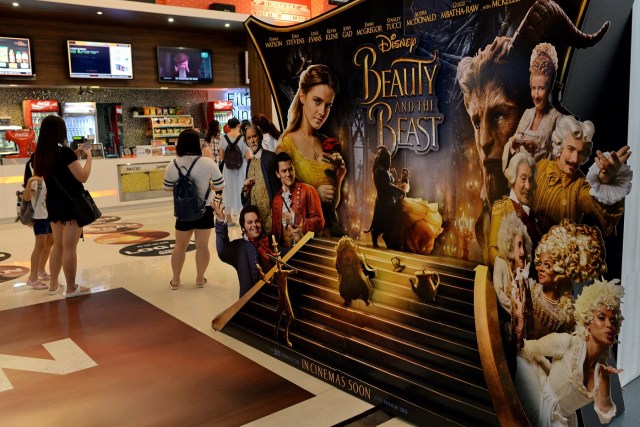 People stand near a promotional display for the film "Beauty and the Beast" at a cinema in Singapore on March 14, 2017. The film has come under fire from religious figures in Singapore, with Christian clergy attacking Disney for deviating from "wholesome, mainstream values". / AFP PHOTO / Roslan RAHMAN