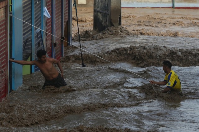 A man helps another man cross a flooded street after a massive landslide and flood in the Huachipa district of Lima, Peru March 17, 2017. REUTERS/Guadalupe Pardo