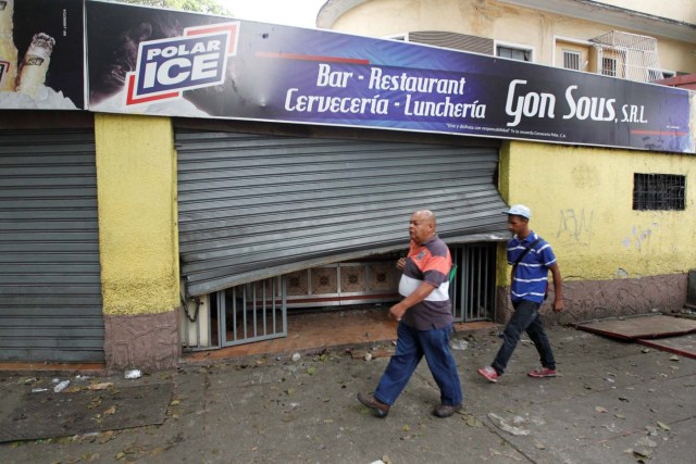 People walk past the damaged entrance of a restaurant after it was looted in Caracas, Venezuela April 20, 2017. REUTERS/Christian Veron
