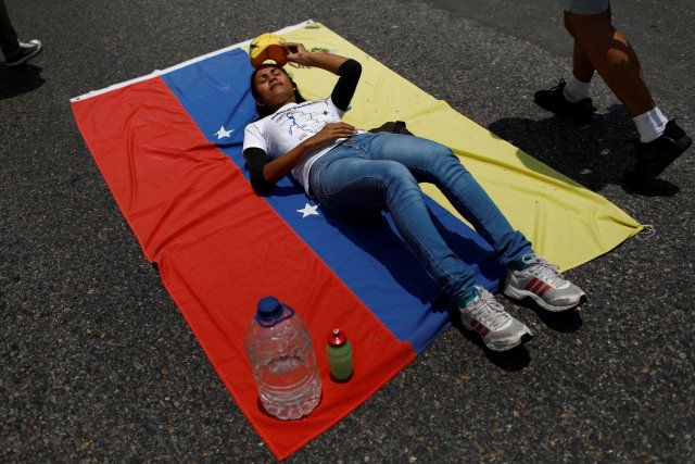 An opposition supporter lies down on the floor over a Venezuelan flag during a rally against Venezuela's President Nicolas Maduro in Caracas