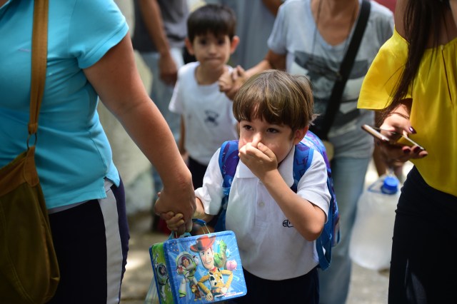 A schoolboy covers his nose and mouth to avoid breathing tear gas shot by police at opponents of Venezuelan President Nicolas Maduro marching in Caracas on April 26, 2017. Protesters in Venezuela plan a high-risk march against President Maduro Wednesday, sparking fears of fresh violence after demonstrations that have left 26 dead in the crisis-wracked country. / AFP PHOTO / RONALDO SCHEMIDT