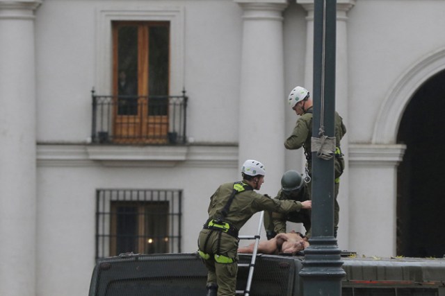 CHI03. SANTIAGO (CHILE), 25/05/2017.- Un hombre desnudo es detenido por la policía chilena luego de que este se lanzara sobre el vehículo policiaco tras trepar el mástil de la bandera chilena en frente del Palacio de La Moneda hoy, jueves 25 de mayo de 2017, en Santiago (Chile). En una inusual protesta, de la que se desconocen hasta el momento los motivos, el hombre permaneció varios minutos en el mástil hasta que se lanzó y cayó sobre un autobús de los carabineros de la policía chilena, quienes aseguraron que el sujeto tiene problemas mentales. EFE/Marcelo Rodríguez