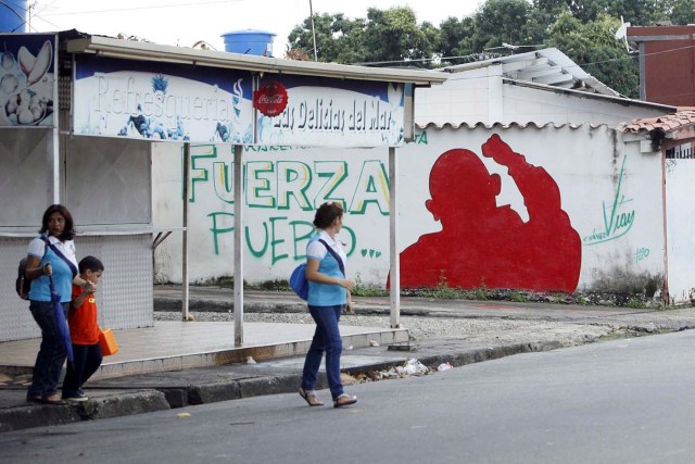 People walk past a mural depicting Venezuela's late President Hugo Chavez that reads, "Strength, people" in Barinas, Venezuela June 12, 2017. Picture taken June 12, 2017. REUTERS/Carlos Eduardo Ramirez
