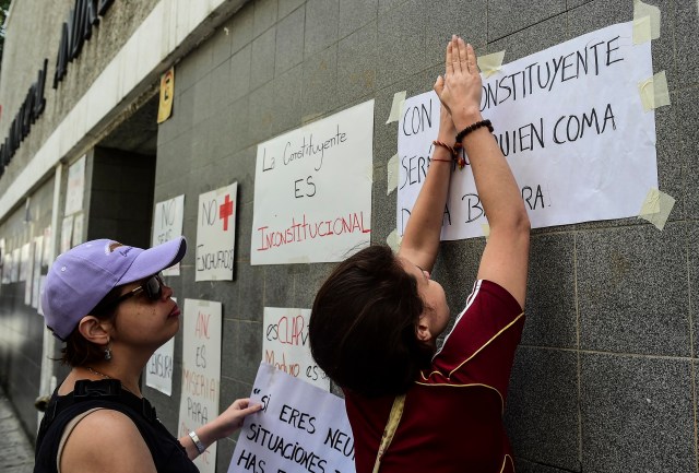  Las mujeres pegan letreros contra el presidente Maduro y su llamado a la Asamblea Constituyente en la pared de una escuela que será utilizada como mesa de votación, en Caracas, el 24 de julio de 2017. La enojada oposición venezolana está presionando por un boicot de una próxima votación que rechaza como una estratagema del presidente Nicolas Maduro para aferrarse al poder./ AFP PHOTO / RONALDO SCHEMIDT