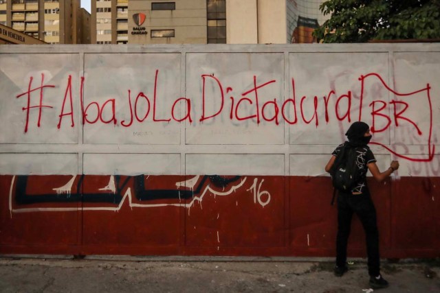 VEN027. CARACAS (VENEZUELA), 18/07/2017.- Un manifestante opositor permanece en frente de un grafiti durante una protesta hoy, martes 18 de julio de 2017, en Caracas (Venezuela). Caracas fue el escenario de nuevas protestas en las que varías vías fueron cerradas por manifestantes opositores que rechazan la Asamblea Nacional Constituyente convocada por el presidente, Nicolás Maduro. La oposición anunció ayer que buscará un gobierno de transición y convocó a una huelga general este jueves para elevar la presión contra la Constituyente promovida por el Ejecutivo. EFE/Miguel Gutiérrez