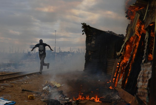 A man runs past a shack which was burnt to the ground by protestors in the Kibera slum in Nairobi on August 12, 2017. Three people, including a child, have been shot dead in Kenya during opposition protests which flared for a second day Saturday after the hotly disputed election victory of President Uhuru Kenyatta. Demonstrations and running battles with police broke out in isolated parts of Nairobi slums after anger in opposition strongholds against August 8 election that losing candidate Raila Odinga claims was massively rigged. / AFP PHOTO / CARL DE SOUZA