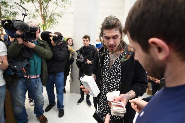 Marco White Jr., son of British chef Marco Pierre White pays cash for his Apple iPhone X after being the first to enter to buy the newly released smartphone at Apple's Regent Street store in central London on November 3, 2017. Apple's flagship iPhone X hit stores on November 3, as the world's most valuable company predicted bumper sales despite the handset's eye-watering price tag and celebrated a surge in profits. The device features facial recognition, cordless charging and an edge-to-edge screen made of organic light-emitting diodes used in high-end televisions. It marks the 10th anniversary of the first iPhone release and is released in about 50 markets around the world. / AFP PHOTO / CHRIS RATCLIFFE