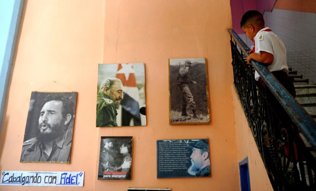A Cuban primary school student looks at a wall decorated with posters of late Cuban leader Fidel Castro in Havana, on November 23, 2017. Cuba commemorates on November 25 the first anniversary of the death of Fidel Castro, focused on an electoral process that will imply a presidential change, in a framework of economic regression, hostility from the United States, and stagnation in its reforms. / AFP PHOTO / YAMIL LAGE