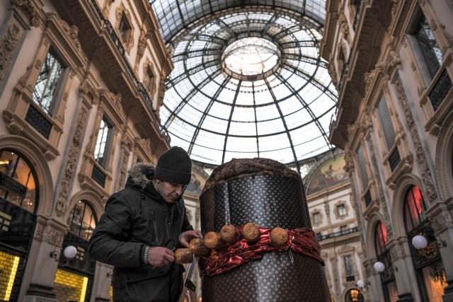 A baker decorates a giant "Panettone" on December 17, 2017 in the Vittorio Emanuele II gallery in Milan. The Panettone, a typical brioche of Christmas in the Lombardy region, is traditionally stuffed with raisins, candied fruits and citrus zest.  / AFP PHOTO / MARCO BERTORELLO