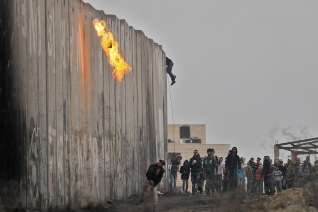 Palestinians throw a cocktail molotov and stones towards Israeli forces on the other side of a barrier at the Qalandia checkpoint in the occupied West Bank on December 20, 2017 as protests continue following the US president's controversial recognition of Jerusalem as Israel's capital. / AFP PHOTO / Thomas COEX