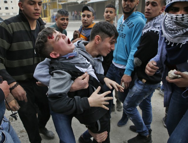 Palestinian protestors carry an injured youth during clashes with Israeli forces near the Qalandia checkpoint in the occupied West Bank on December 20, 2017 as protests continue following the US president's controversial recognition of Jerusalem as Israel's capital.  / AFP PHOTO / ABBAS MOMANI