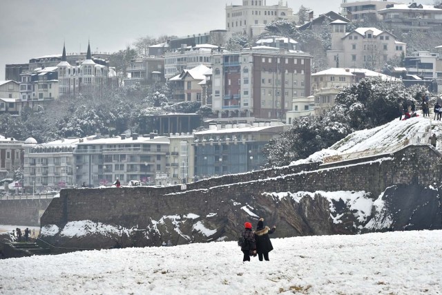 People walk on the beach covered with snow after a heavy snowfall in San Sebastian, northern Spain, on February 28, 2018. School was cancelled across swathes of Europe as a blast of Siberian weather dubbed the "Beast from the East" kept the mercury far below zero. / AFP PHOTO / ANDER GILLENEA
