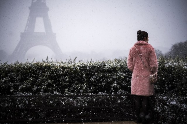 A woman stands under the snow on the Place du Trocadero in front the Eiffel Tower in Paris on February 5, 2018. / AFP PHOTO / Lionel BONAVENTURE