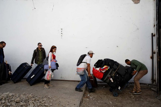 Karelys Betancourt (C) looks at men pushing a cart loaded with luggage which belongs to people traveling by bus from Caracas to Ecuador in San Antonio del Tachira, Venezuela, November 8, 2017. Since 2015, vehicular traffic between Venezuela and Colombia has been restricted, so the first stage of the trip ends in the Venezuelan border city of San Antonio de Tachira. There, travelers have to leave the first bus and carry all their luggage as they cross by feet to the Colombian side, after going through several customs checkpoints and getting their passport stamped. REUTERS/Carlos Garcia Rawlins SEARCH "RAWLINS BUS" FOR THIS STORY. SEARCH "WIDER IMAGE" FOR ALL STORIES.