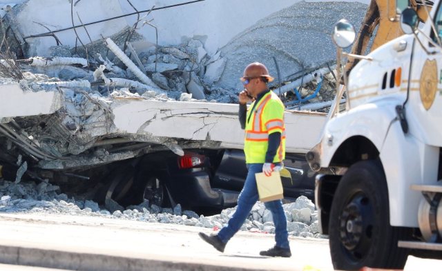 A worker walks past a car beneath a collapsed pedestrian bridge at Florida International University in Miami, Florida, U.S., March 16, 2018.  REUTERS/Joe Skipper