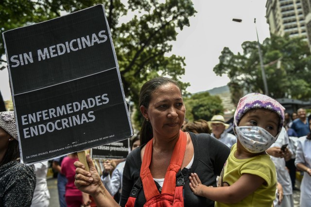 A woman with her sick daughter takes part in a protest by health workers and patients for the lack of medicines, medical supplies and poor conditions in hospitals, in Caracas on April 17, 2018.  Doctors and nurses protest against the health crisis in Venezuela, currently in the midst of a deep economic and political crisis and where health authorities have reported a rise in vaccine-preventable diseases. / AFP PHOTO / Luis ROBAYO