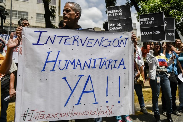 A man holds a placard reading "Humanitarian Intervention Now" during a protest by health workers and patients for the lack of medicines, medical supplies and poor conditions in hospitals, in Caracas on April 17, 2018. Doctors and nurses protest against the health crisis in Venezuela, currently in the midst of a deep economic and political crisis and where health authorities have reported a rise in vaccine-preventable diseases. / AFP PHOTO / Luis ROBAYO