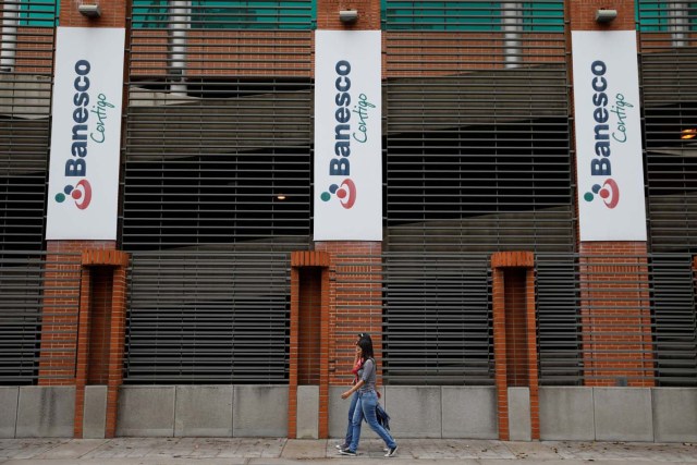 People walk past corporate logos of Banesco bank at one of their office complexes in Caracas, Venezuela May 3, 2018. REUTERS/Carlos Garcia Rawlins