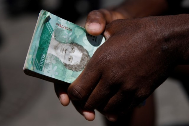 Un vendedor callejero sostiene un fajo de billetes de bolívares mientras espera a clientes en Caracas. Imagen de archivo. 23 de marzo de 2018. REUTERS/Carlos Garcia Rawlins