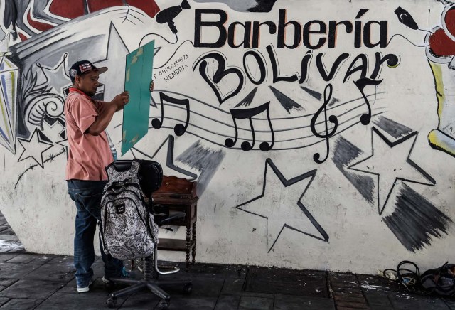 Un hombre ofrece cortes de pelo debajo de un puente en Caracas el 28 de mayo de 2018. Bajo un puente o en un mercado al aire libre en Caracas, los peluqueros se ganan la vida con herramientas simples y ofrecen cortes de cabello para aquellos que no pueden pagar un salón de belleza debido a un salón de belleza debido a la crisis económica. / AFP PHOTO / Juan BARRE